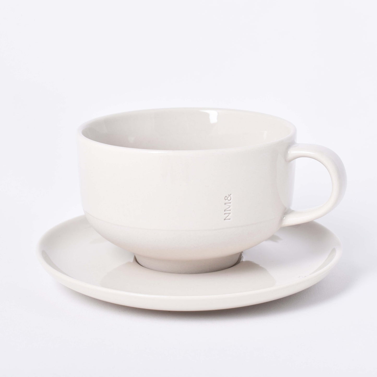 Sandfärgad kopp på runt fat med NM& monogram ingraverat i mitten i design av Carina Seth Andersson