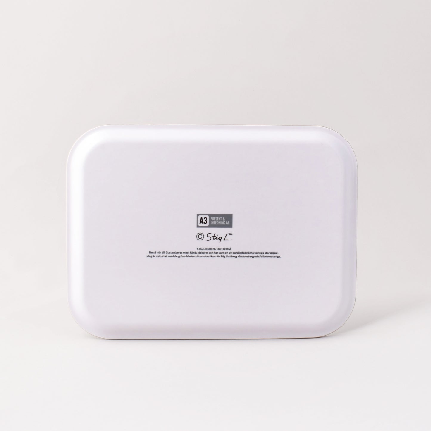 Vit baksida av bricka med Stig Lindbergs signatur