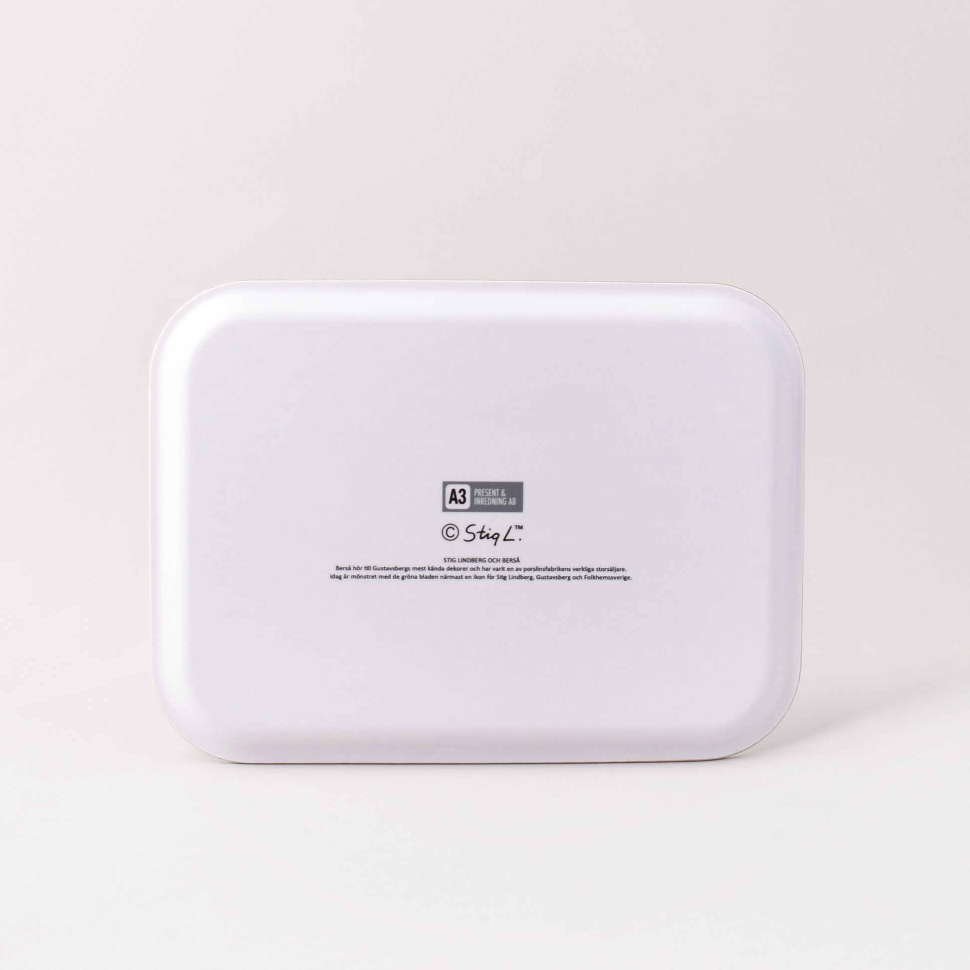 Vit baksida av bricka med Stig Lindbergs signatur