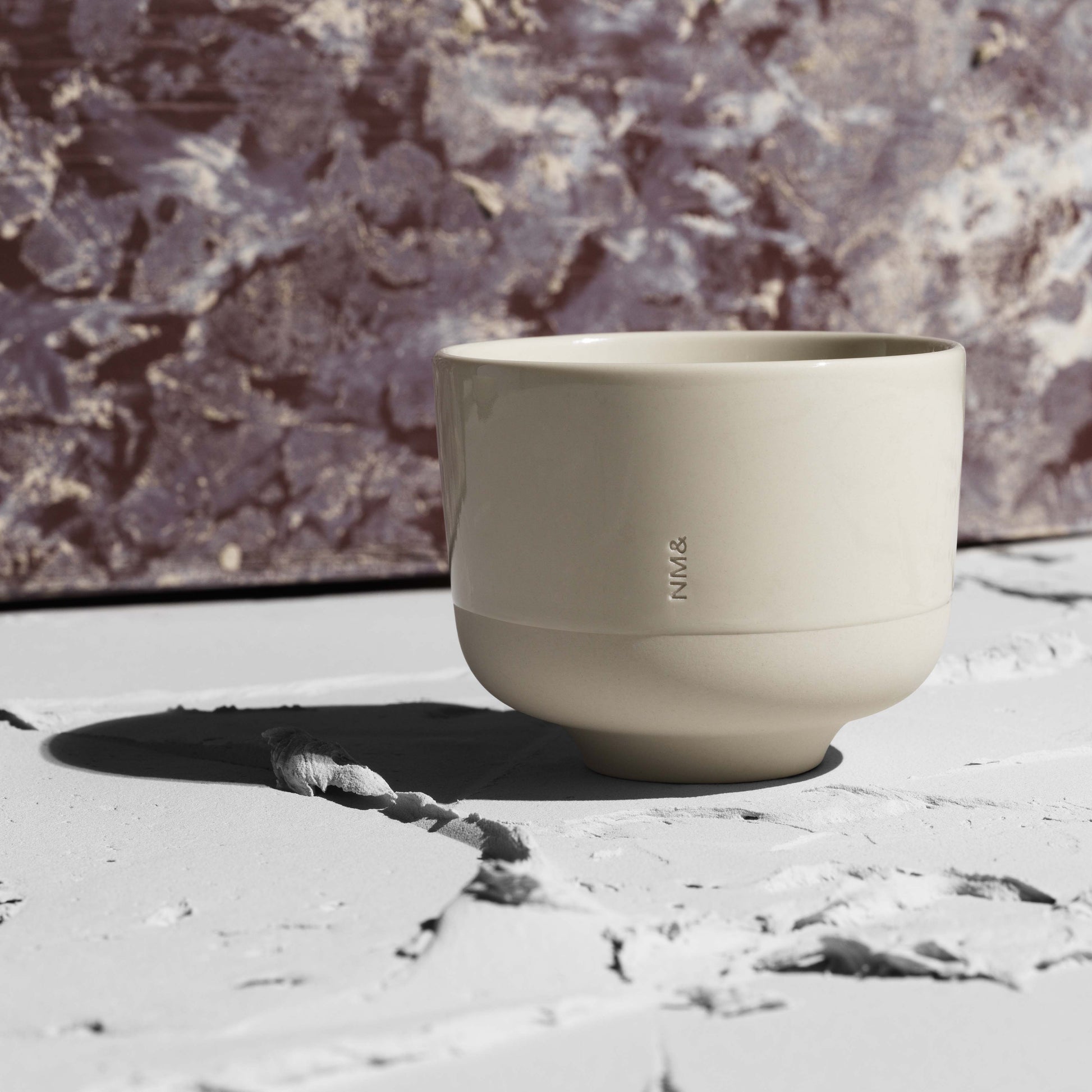 Sandfärgad kopp utan öra framför vägg i röd marmor