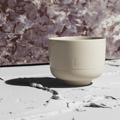 Sandfärgad kopp utan öra framför vägg i röd marmor