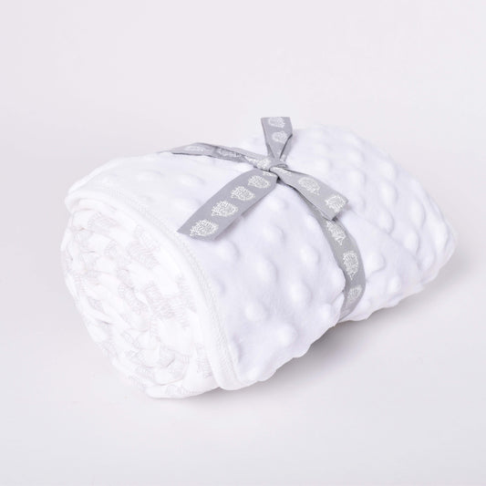 Vit babyfilt med motiv av igelkottar i mönsterdesign av Lisa Larson, hoprullad med grå rosett