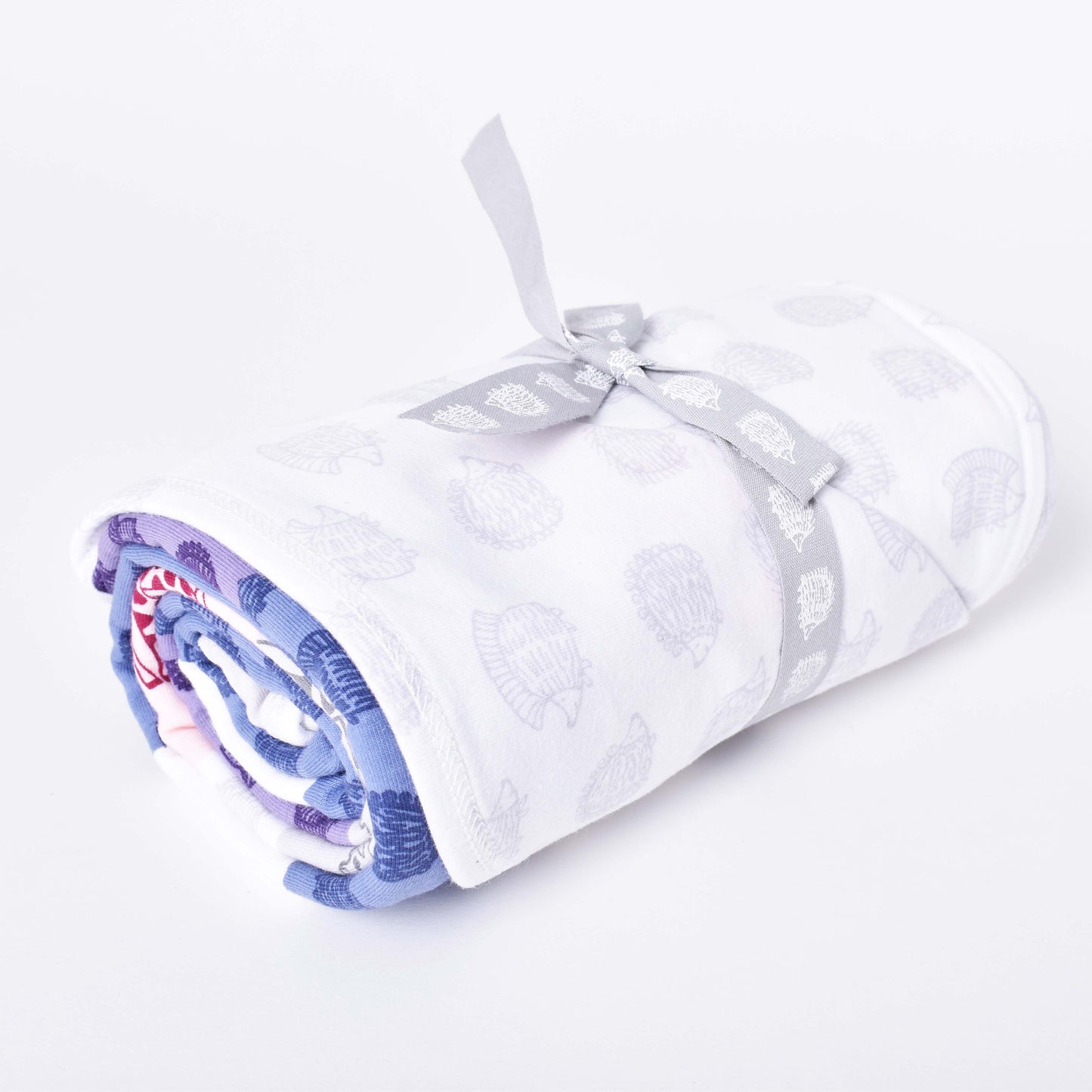 Flerfärgad babyfilt med motiv av igelkottar och giraffer i mönsterdesign av Lisa Larson, ihoprullad med rosett.