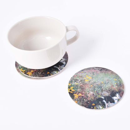 En vit kaffekopp på runt glasunderlägg med motiv av Bruno Liljefors Katt på blomsteräng