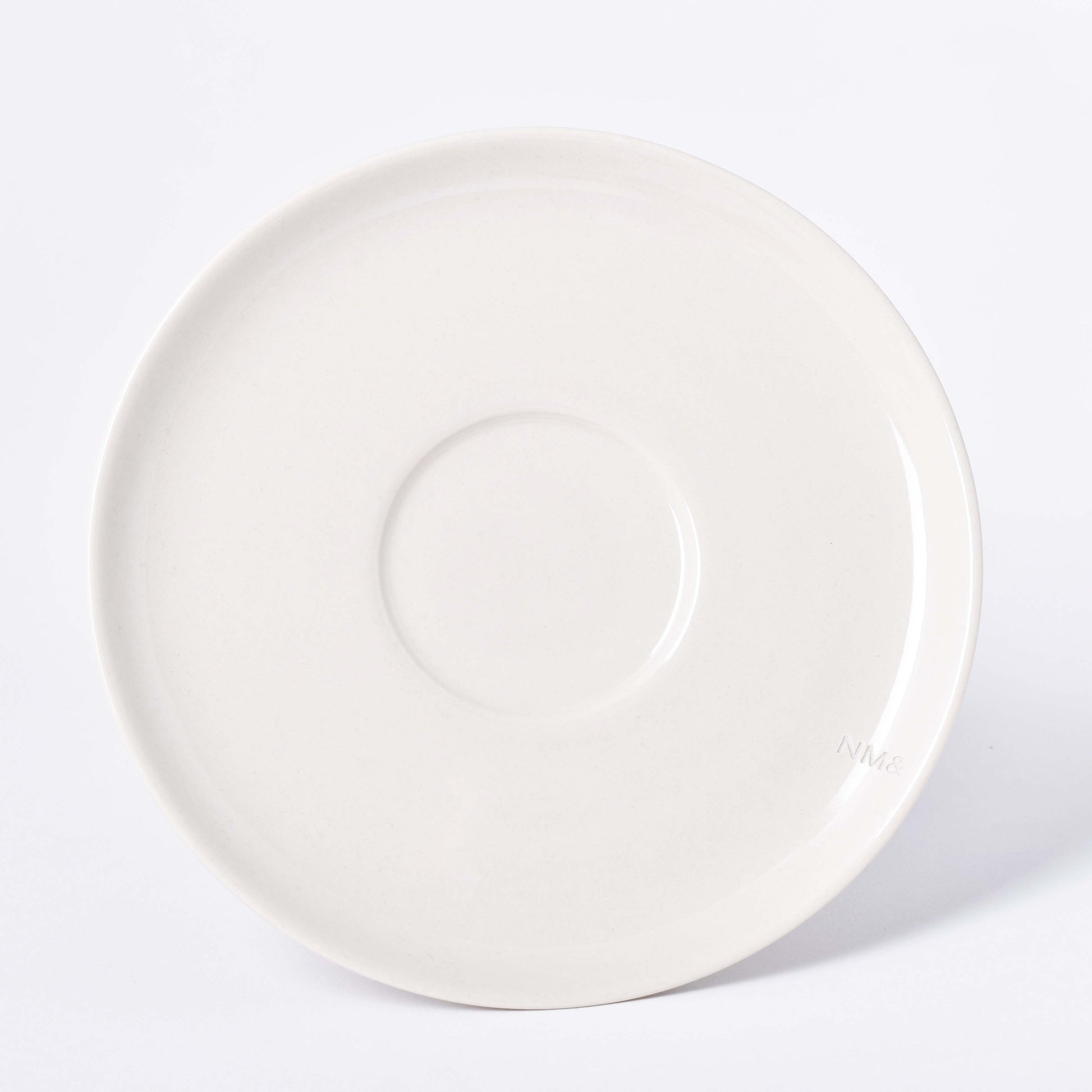 Runt sandfärgat fat till kopp med NM& monogram ingraverat i kanten i design av Carina Seth Andersson