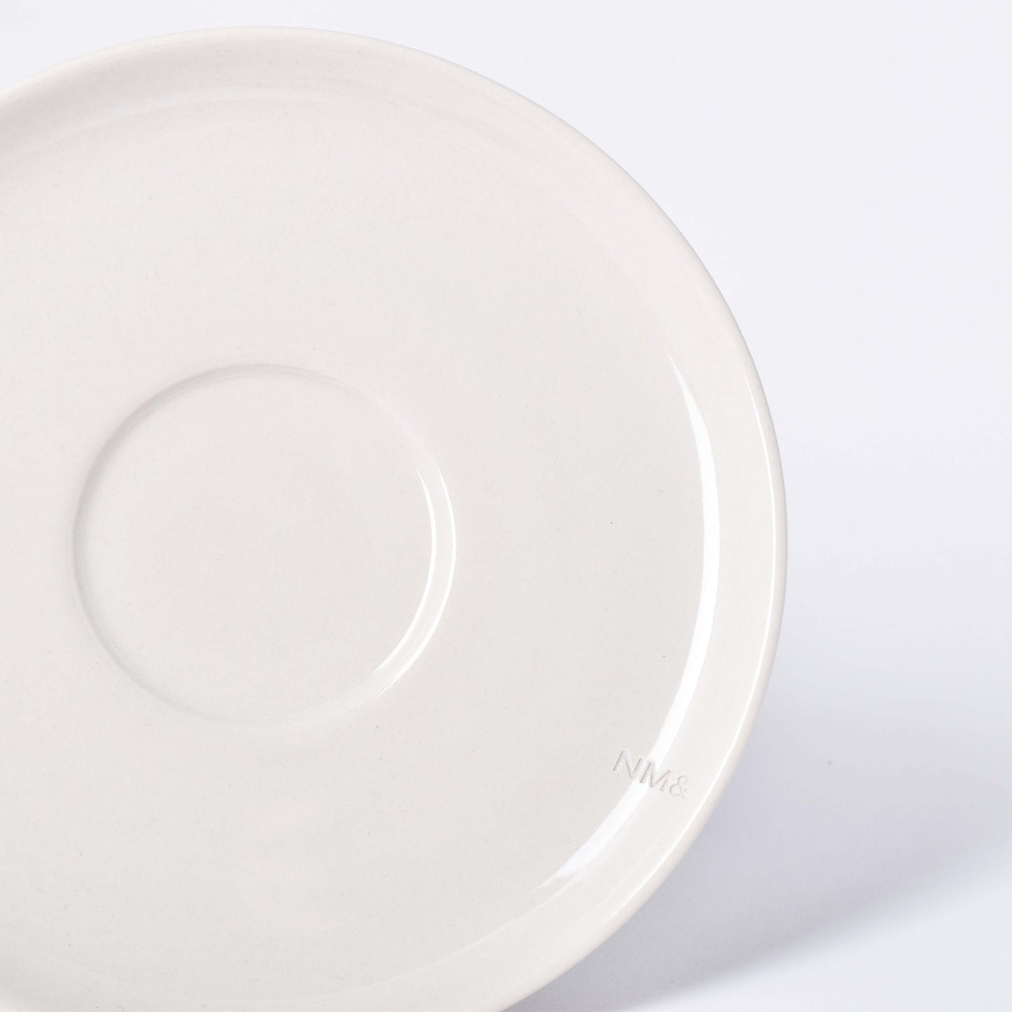 Runt sandfärgat fat till kopp med NM& monogram ingraverat i kanten i design av Carina Seth Andersson