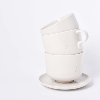 Tre sandfärgade koppar med ingraverat NM& monogram staplade på ett runt fat i design av Carina Seth Andersson