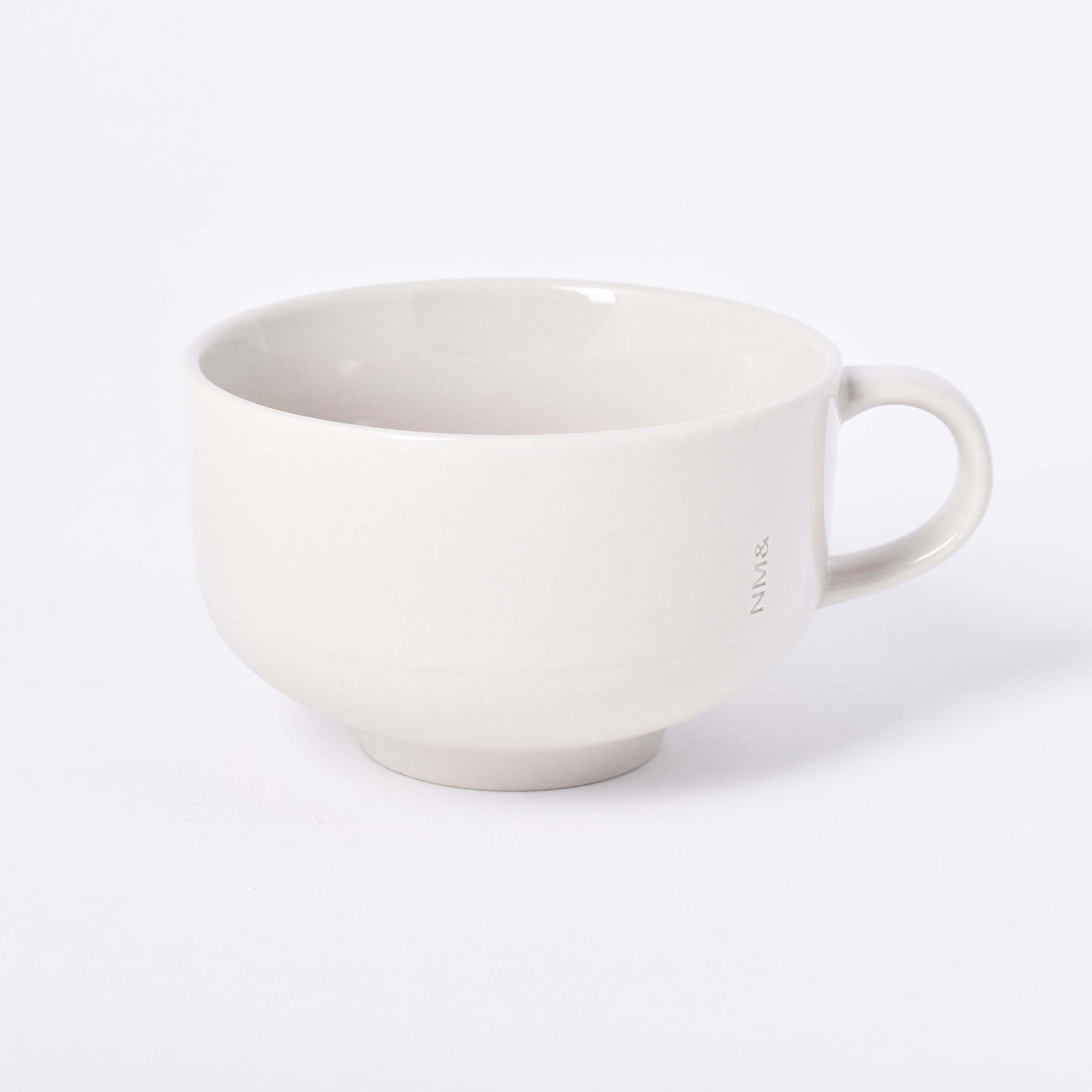 Sandfärgad kopp med öra och NM& monogram ingraverat i mitten i design av Carina Seth Andersson