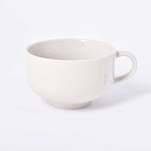 Sandfärgad kopp med öra och NM& monogram ingraverat i mitten i design av Carina Seth Andersson