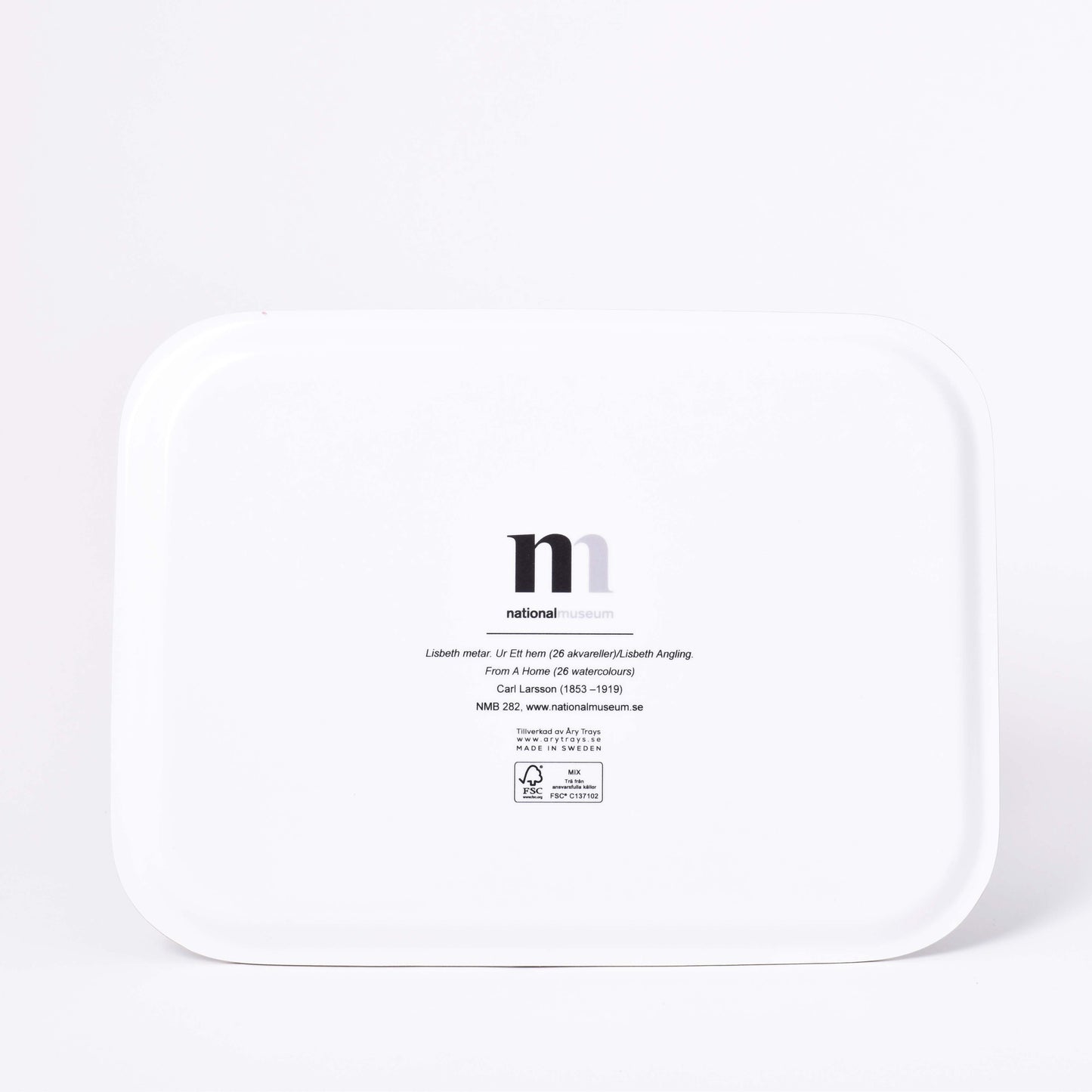 Vit baksida av rektangulär bricka med motiv av Carl Larssons Frukost under stora björken