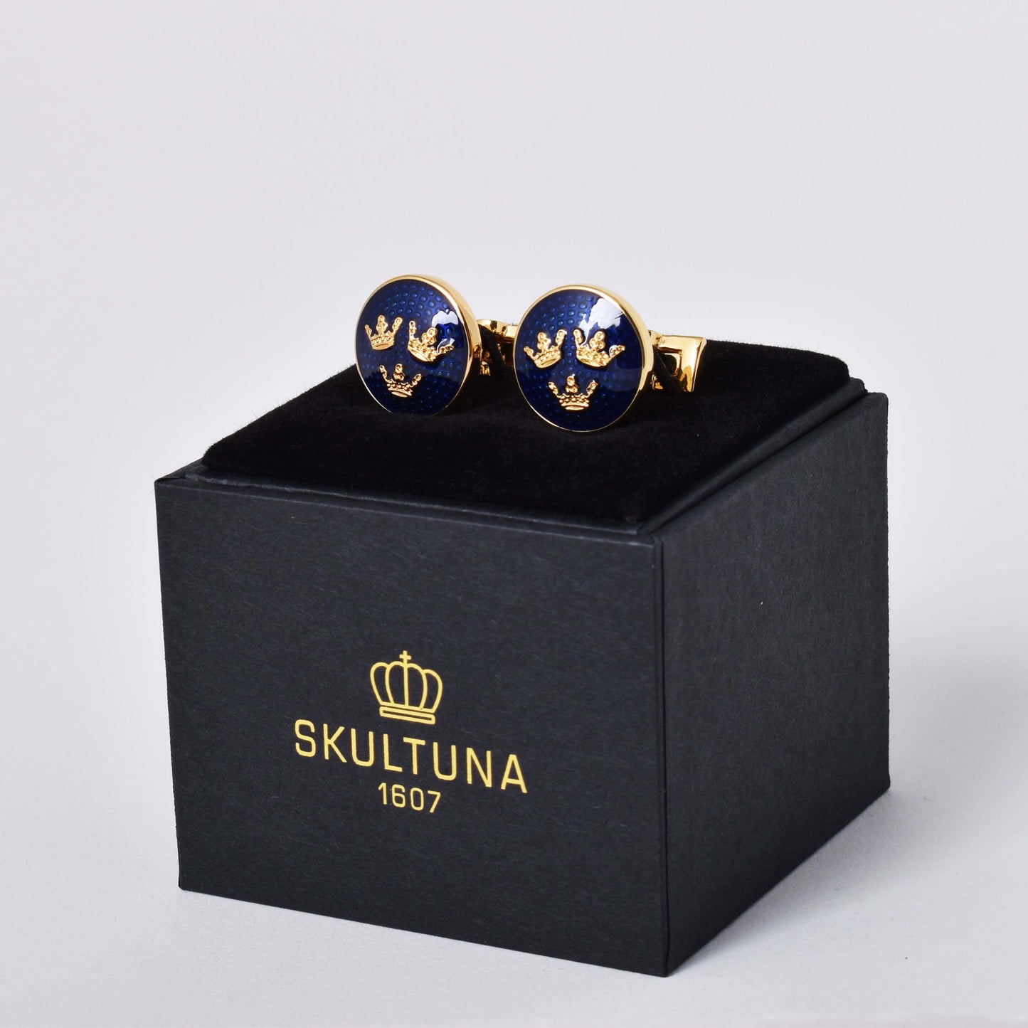 Skultuna manschettknappar med guldpläterad dekor av en variant av riksvapnet Tre Kronor mot kungsblå emalj