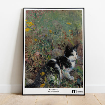 Poster med katt på blomsteräng i svart ram lutad mot en vägg